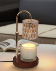 A lit crystal candle warmer lamp melting a scented jar candle on a coffee table with an open magazine and modern sofa in the background.