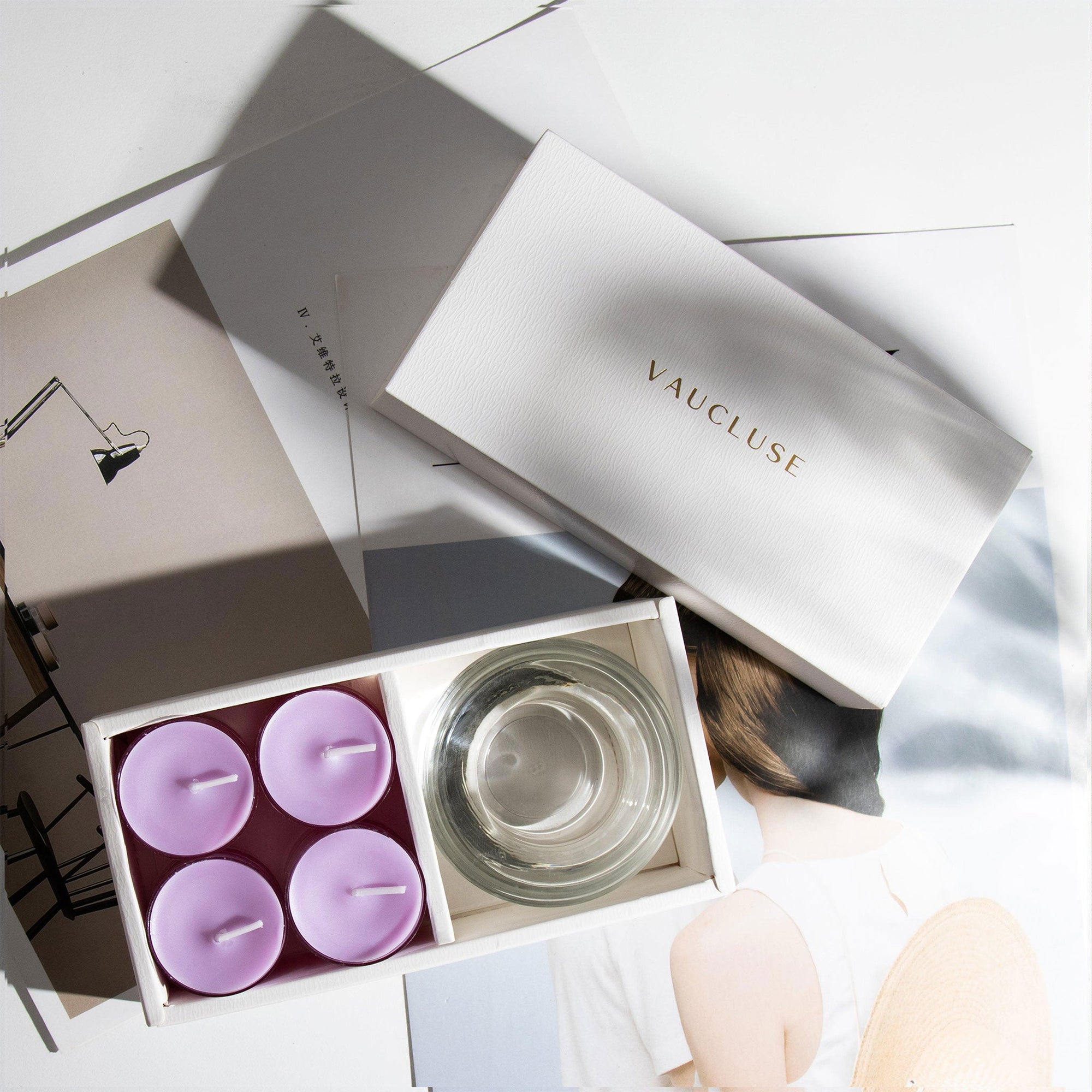 Overhead modern view of the premium lavender scented tealight candle gift box arranged neatly over design books and minimalist editorial magazines.