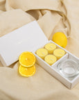 Elegant lifestyle scene showing the lemon tealight aromatherapy gift set styled on draped beige linen fabric with fresh lemon accents.