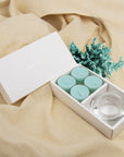 Relaxing lifestyle scene showing the light blue ocean tealight set and clear glass holder resting on textured beige linen fabric next to sea coral decor.