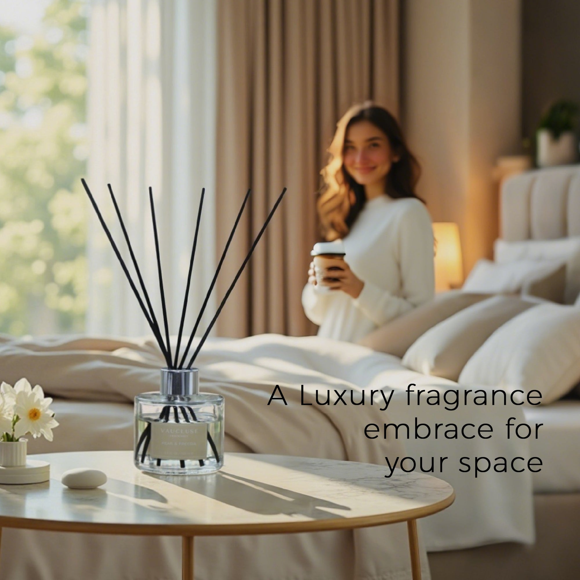A luxury Vaucluse reed diffuser placed on a modern bedside table with a soft-focus background of a woman holding a warm beverage in a beautifully styled beige bedroom.