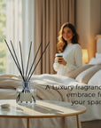 A luxury Vaucluse reed diffuser placed on a modern bedside table with a soft-focus background of a woman holding a warm beverage in a beautifully styled beige bedroom.