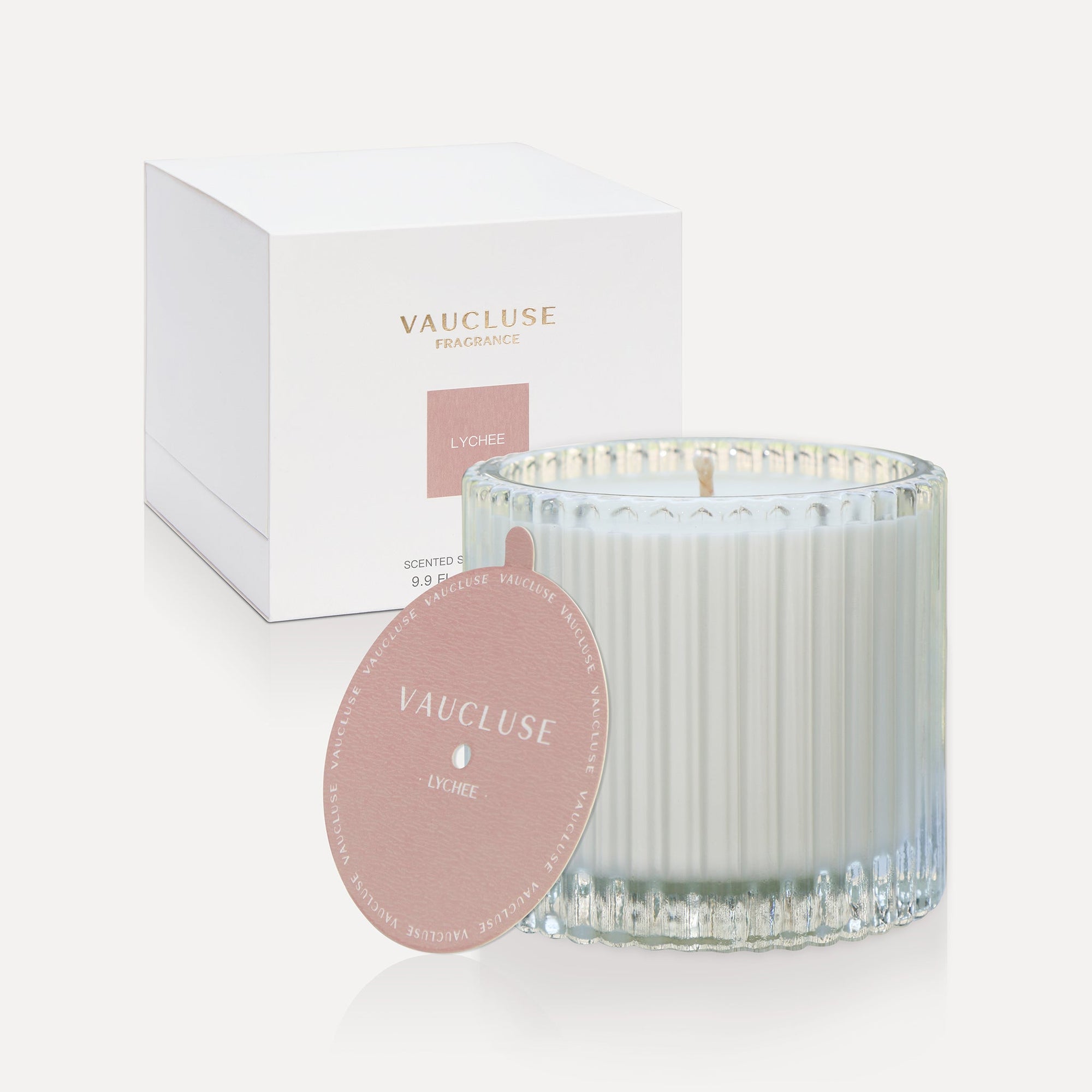 Vaucluse Lychee luxury scented soy wax candle in a clear ribbed glass tumbler jar displayed next to its rose pink dust cover lid and minimalist white gift box.