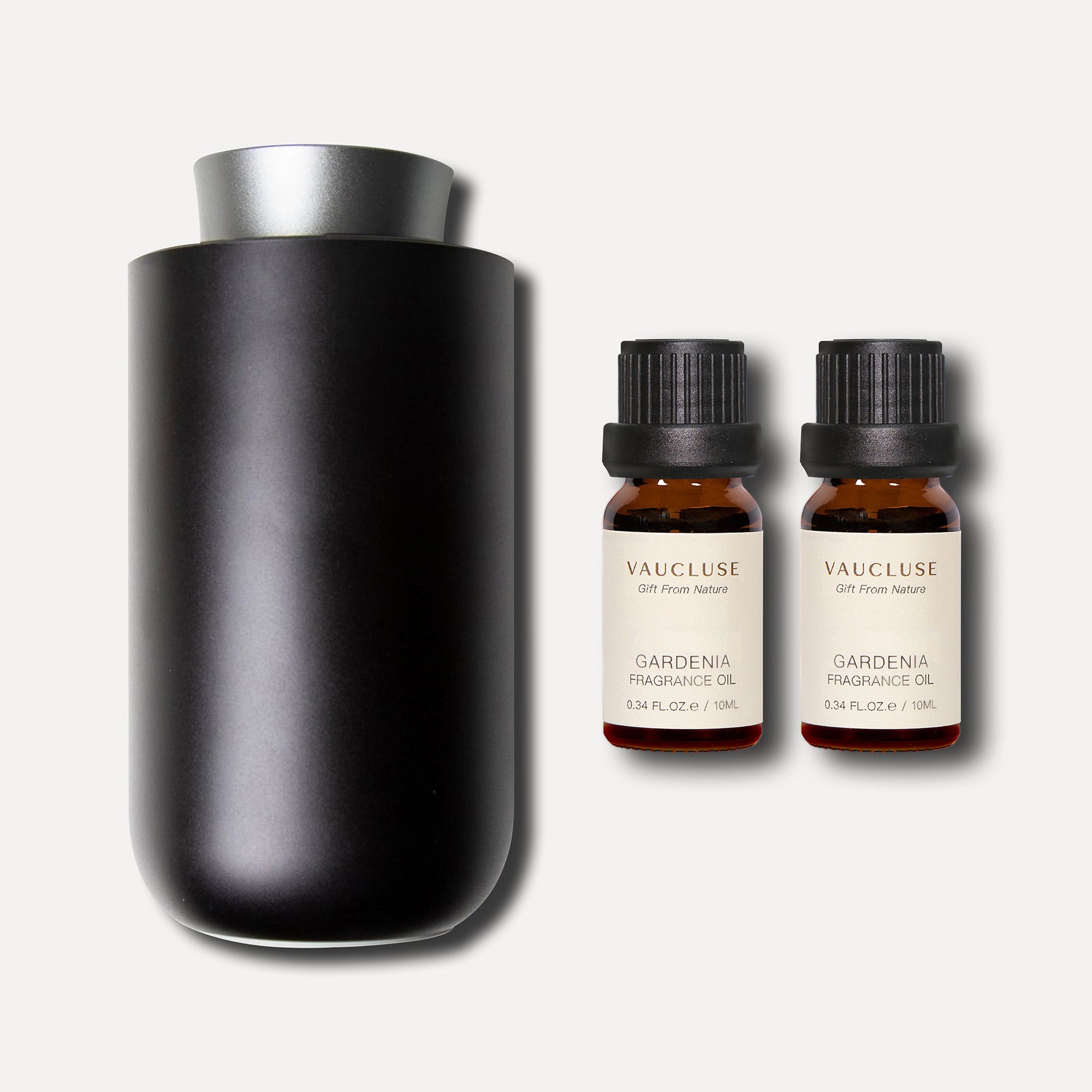A sleek matte black waterless nebulizing diffuser placed next to two 10ml bottles of gardenia essential oil.