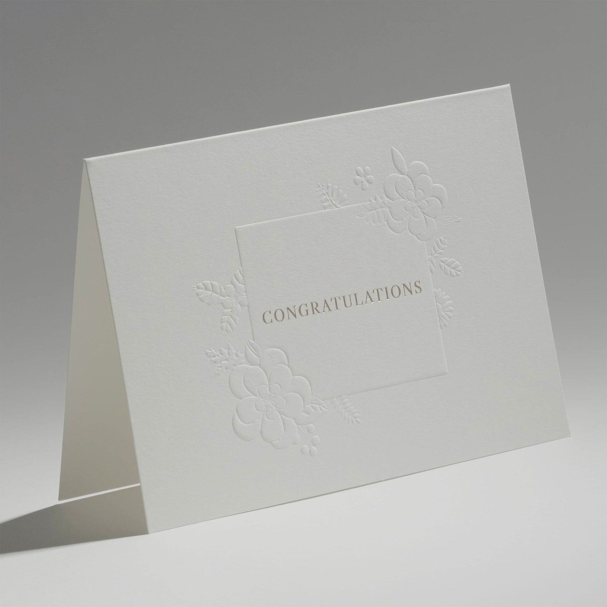 An elegant, freestanding white congratulations card showcasing a detailed debossed floral motif framing the central greeting.