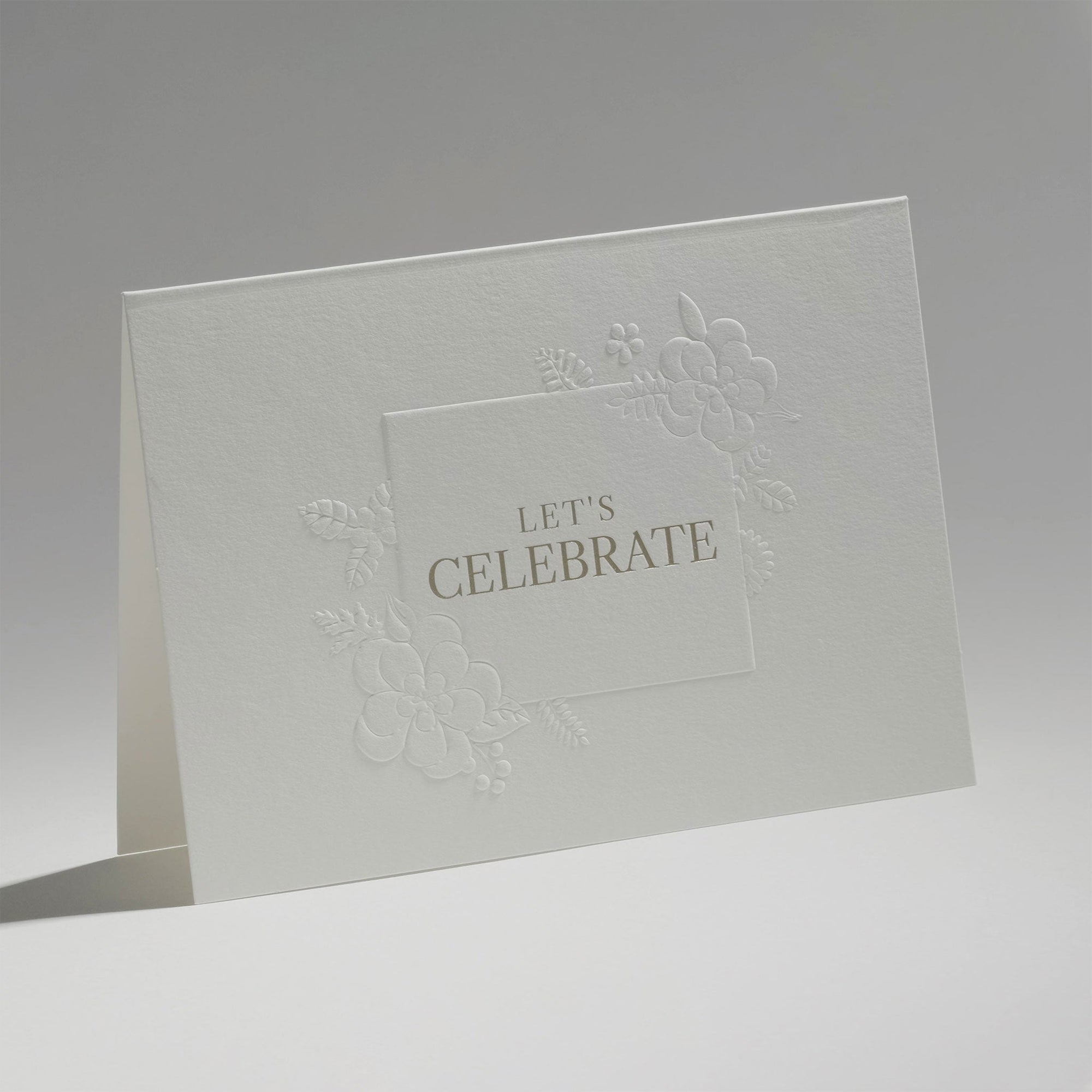 An elegant, freestanding white congratulations greeting card showcasing a detailed blind-embossed floral frame around the central gold typography.