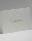 An elegant, freestanding white congratulations greeting card showcasing a detailed blind-embossed floral frame around the central gold typography.