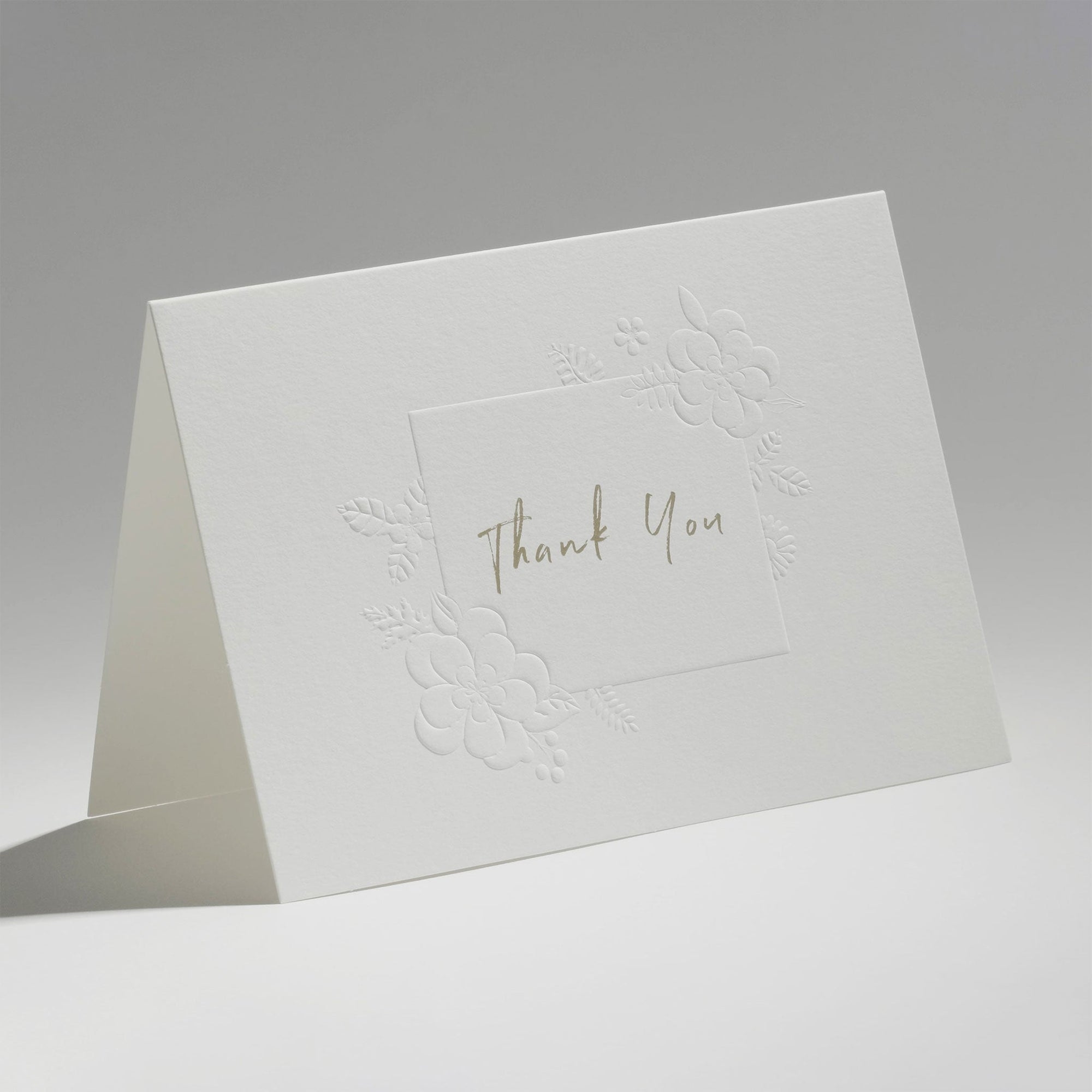 An elegant, freestanding white thank you card showcasing a delicate blind-embossed floral frame around elegant central script text.