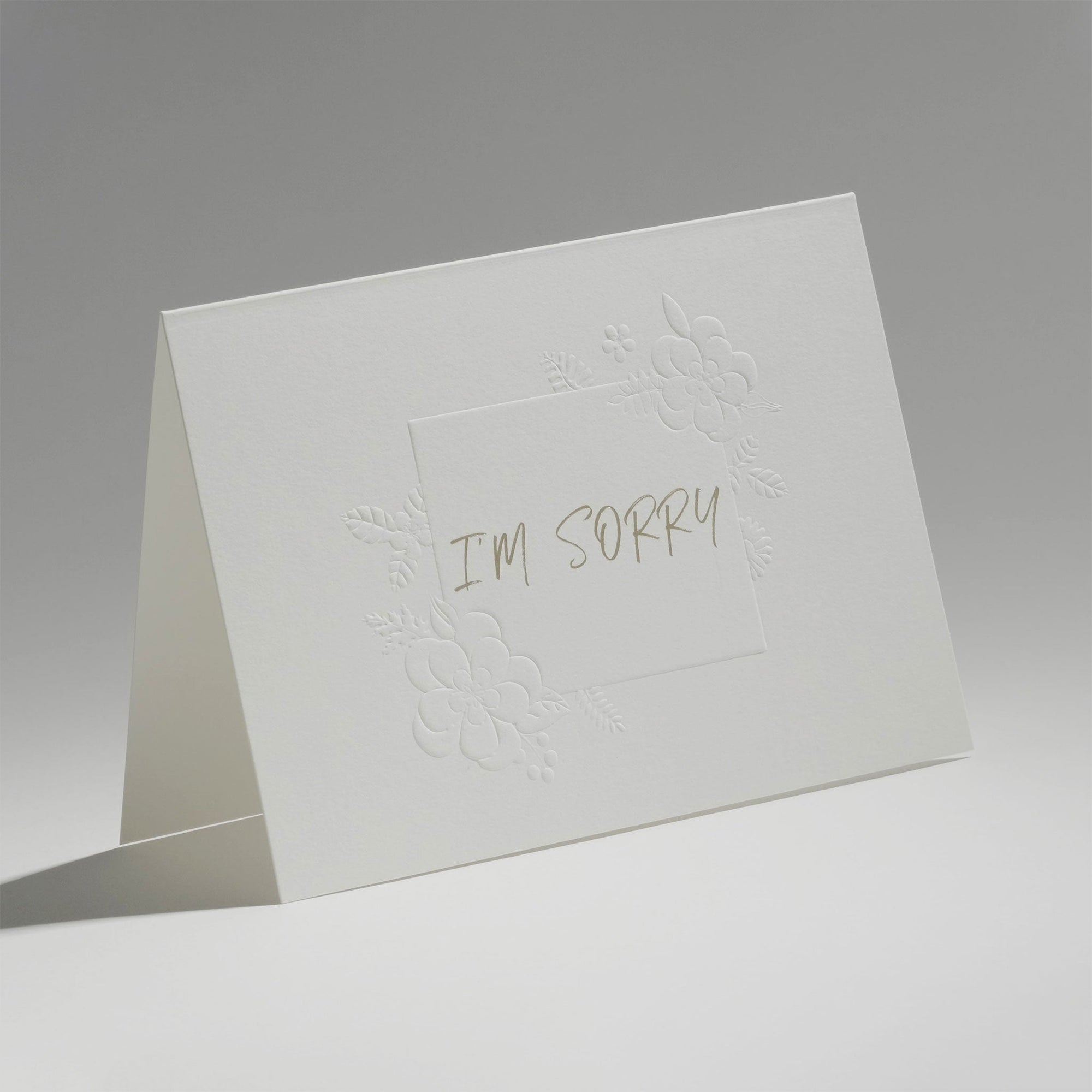 An elegant, freestanding white apology greeting card featuring the text "I'm Sorry" centered within a delicate embossed floral border.
