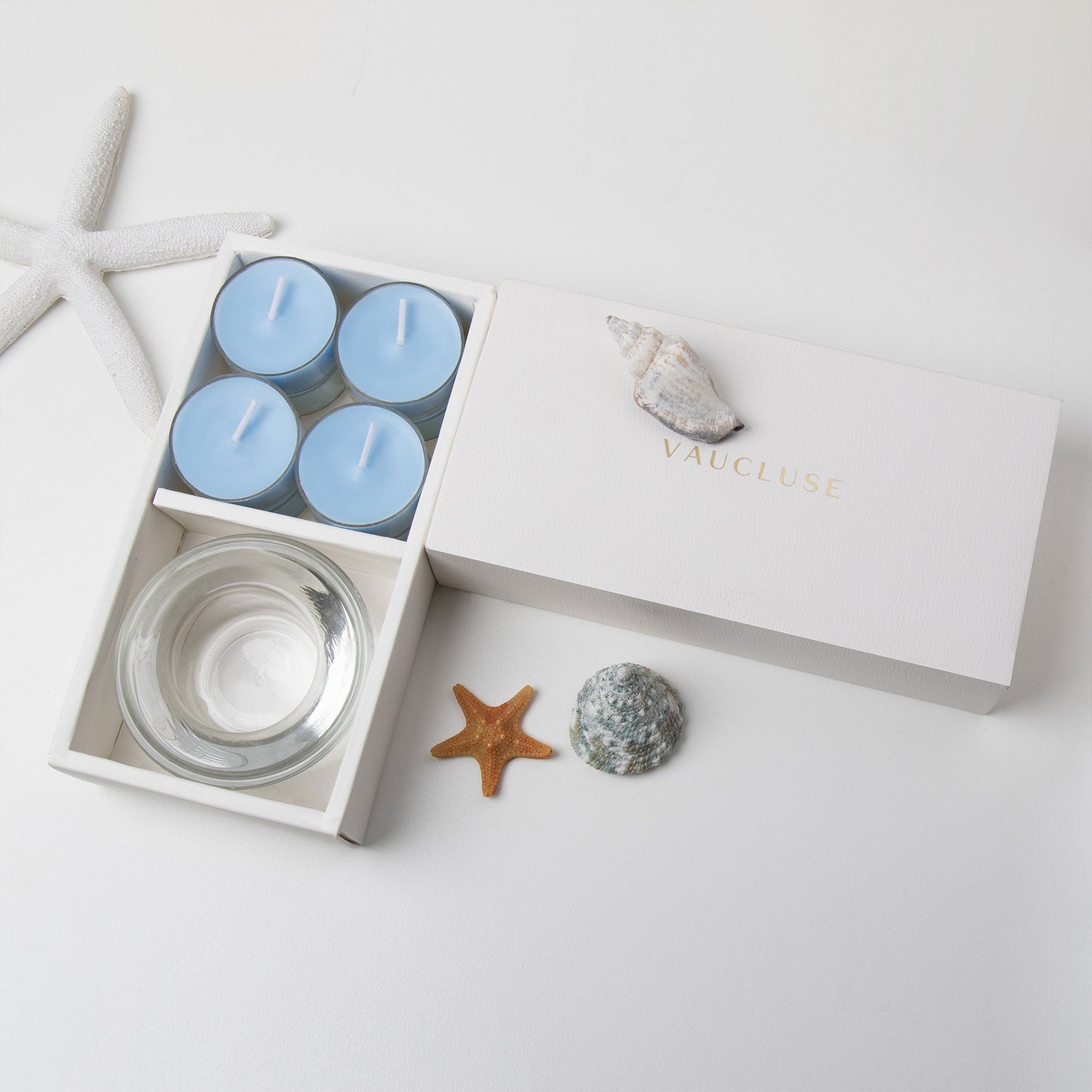 Minimalist overhead flat lay of the open light blue tealight candle set styled with a starfish and decorative seashells on a white background.