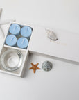 Minimalist overhead flat lay of the open light blue tealight candle set styled with a starfish and decorative seashells on a white background.