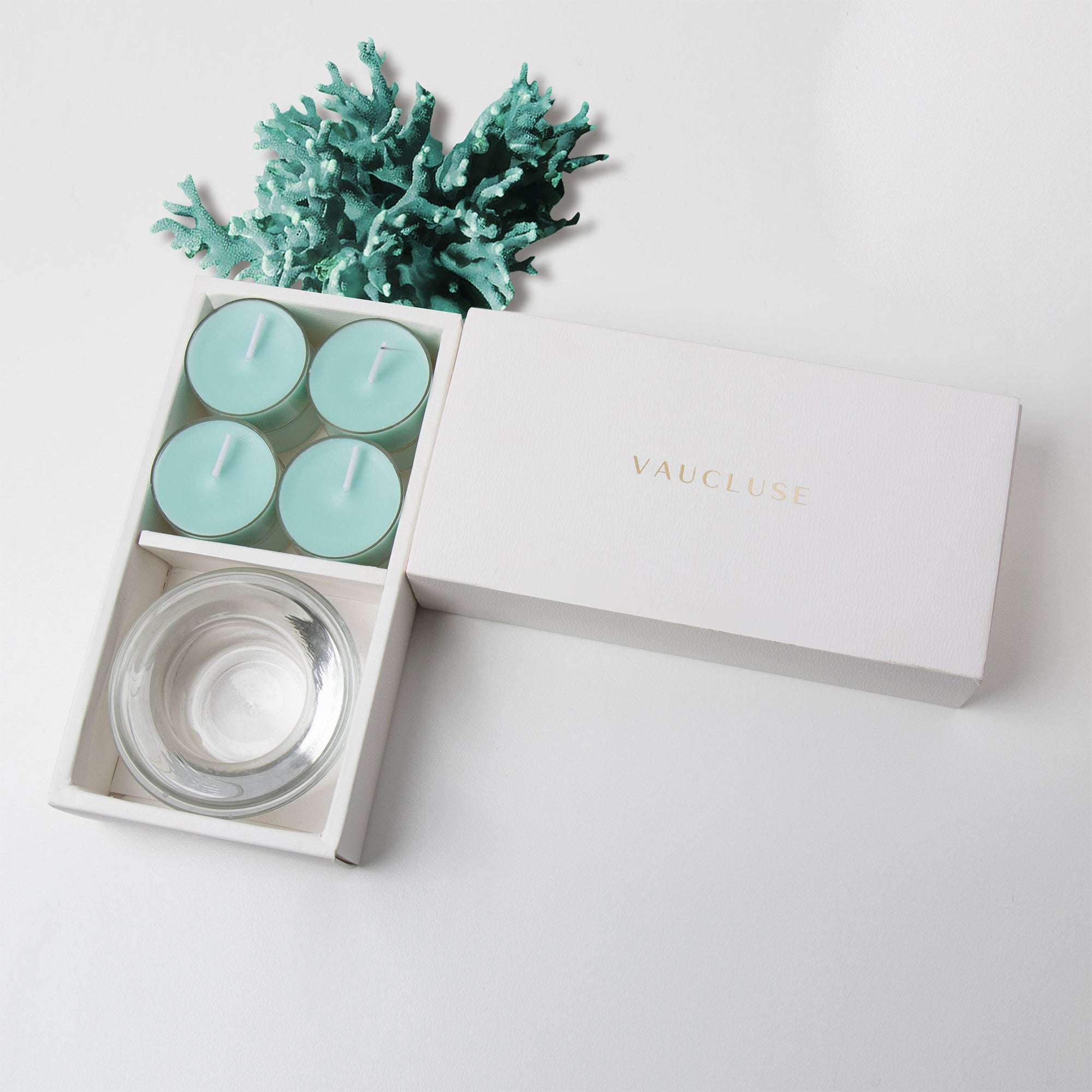 Minimalist overhead flat lay of the open aqua tealight candle set styled beautifully with a piece of decorative teal blue sea coral on a white surface.