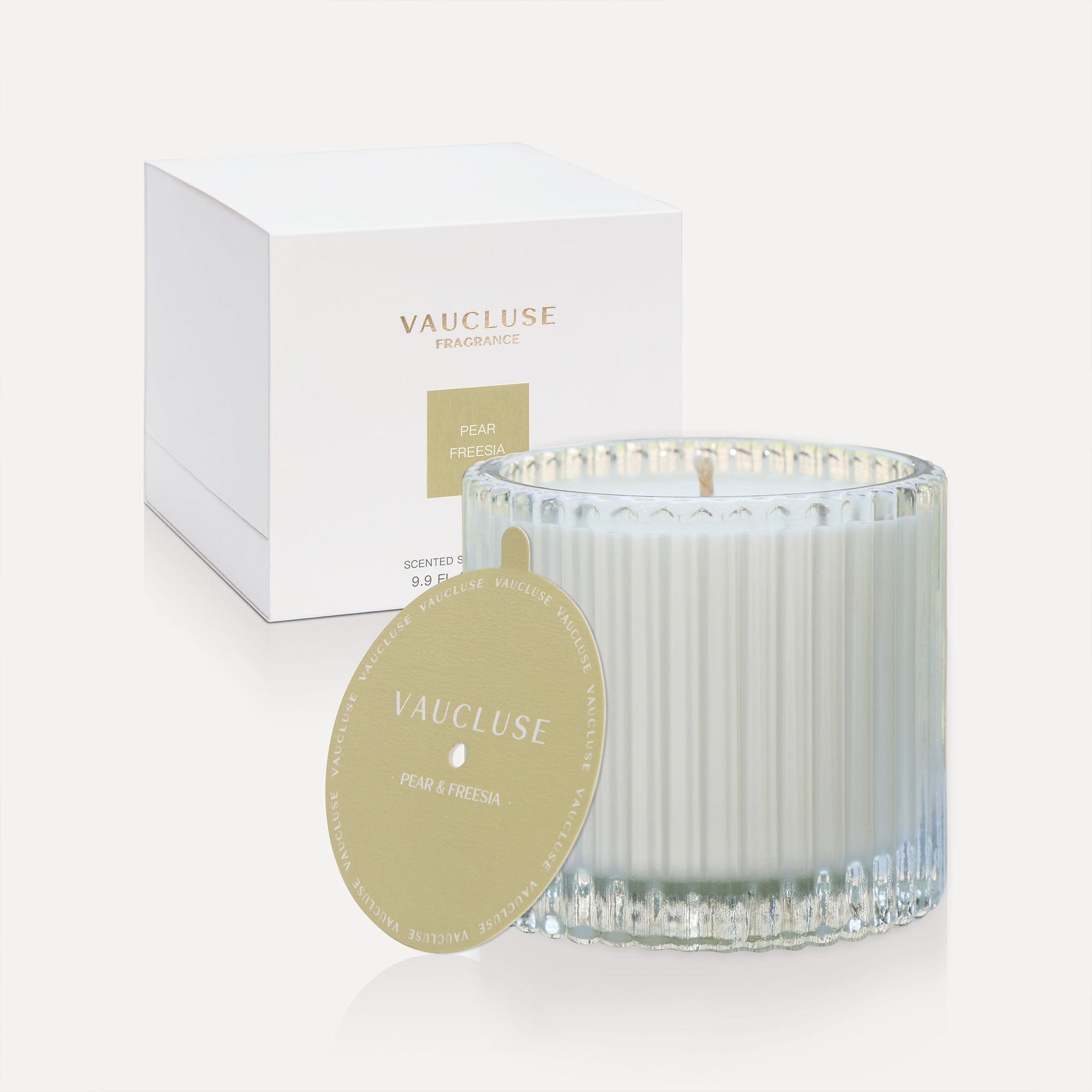 Vaucluse Pear and Freesia luxury scented soy wax candle in a clear ribbed glass tumbler glass jar alongside its minimalist white gift box and gold dust cover lid