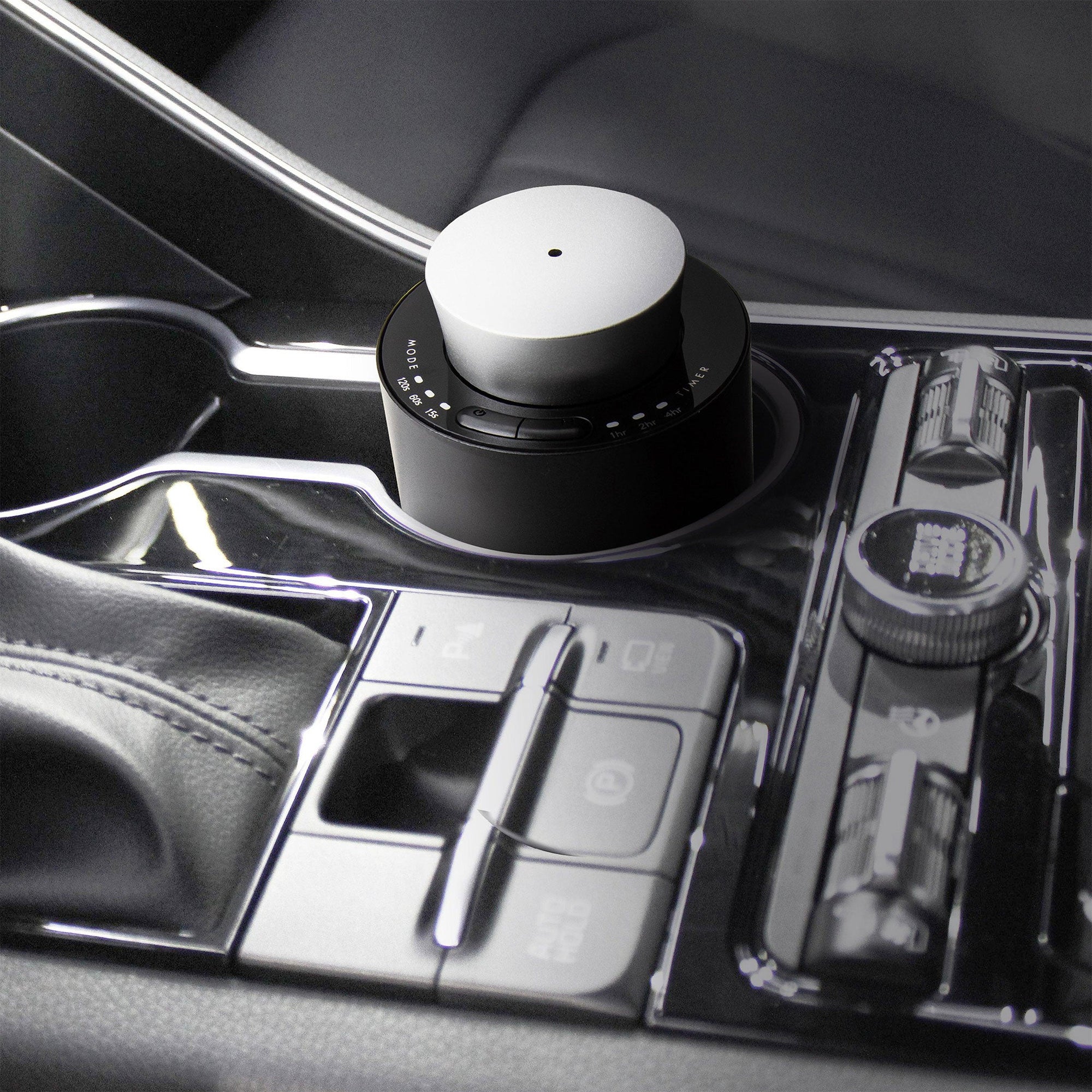 A portable black and silver electronic diffuser resting securely inside a luxury car cup holder console for mobile aromatherapy.
