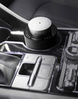 A portable black and silver electronic diffuser resting securely inside a luxury car cup holder console for mobile aromatherapy.