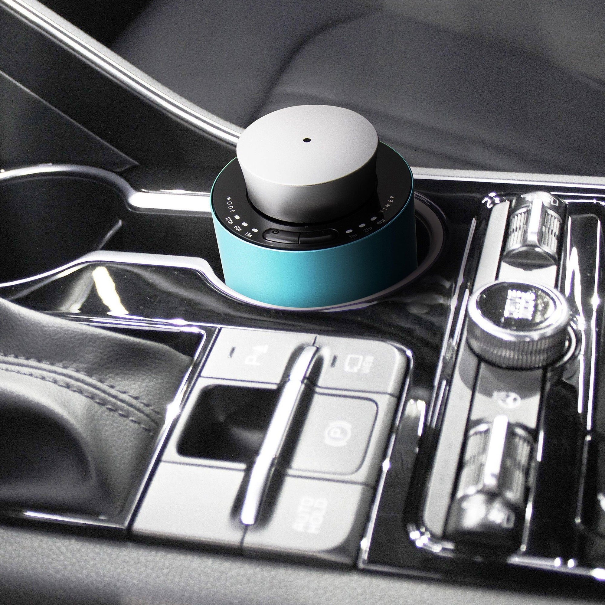 A portable teal and silver electronic diffuser resting securely inside a luxury car cup holder console for mobile aromatherapy.