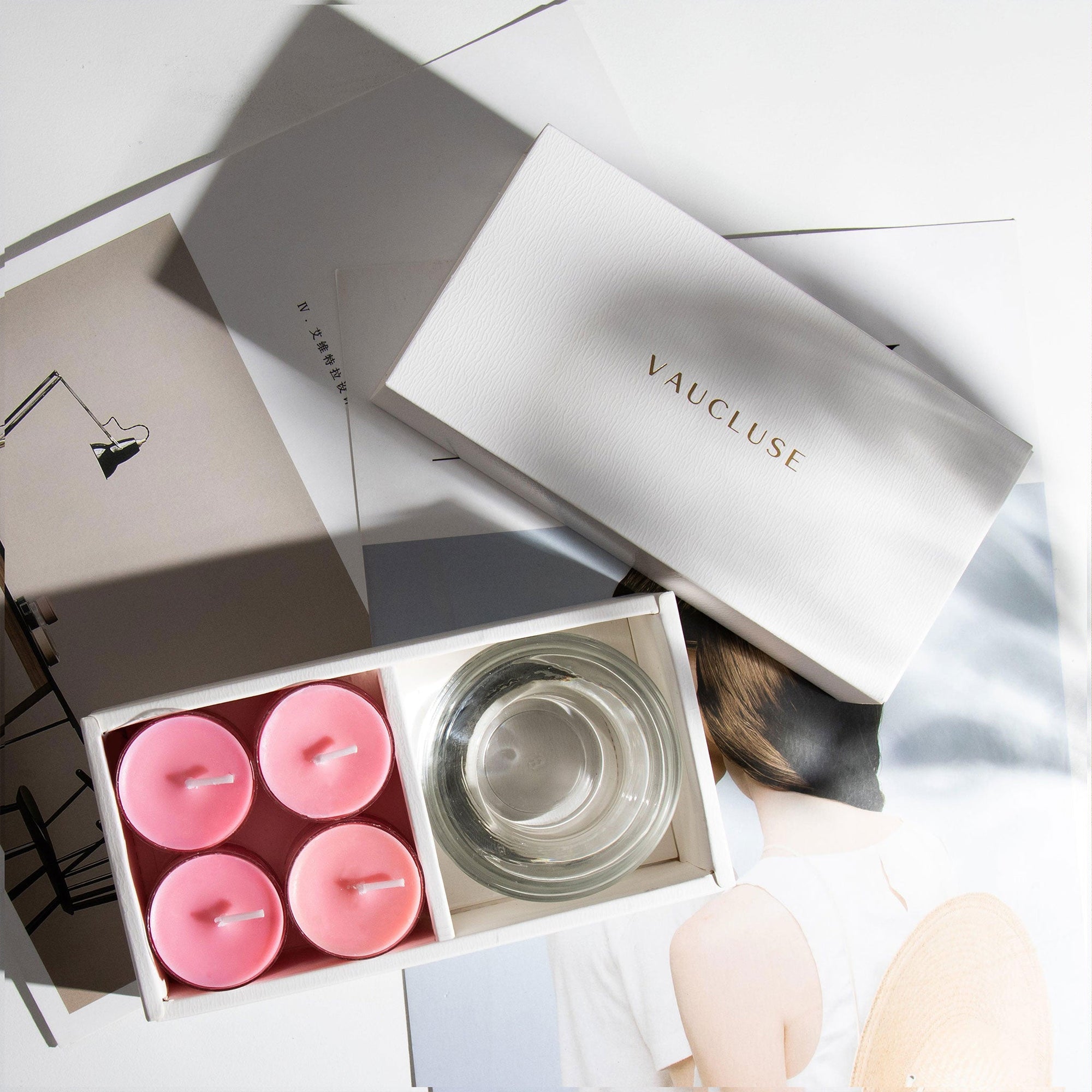 Overhead minimalist view of the open pink rose scented tealight candle gift set arranged over editorial style design books and magazines.