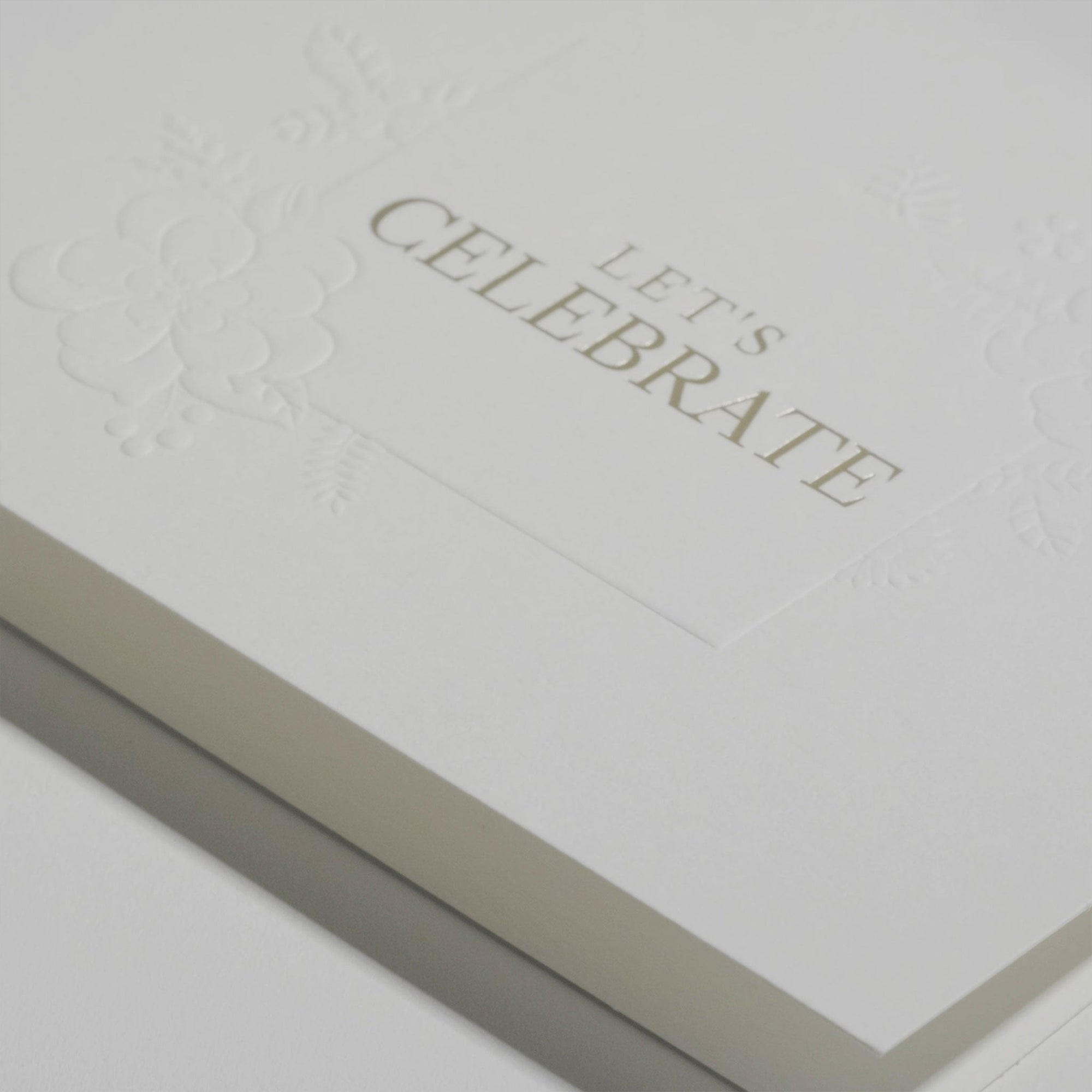 Close-up macro shot highlighting the heavy textured cotton paper and fine gold metallic lettering on the Vaucluse luxury Let's Celebrate card.