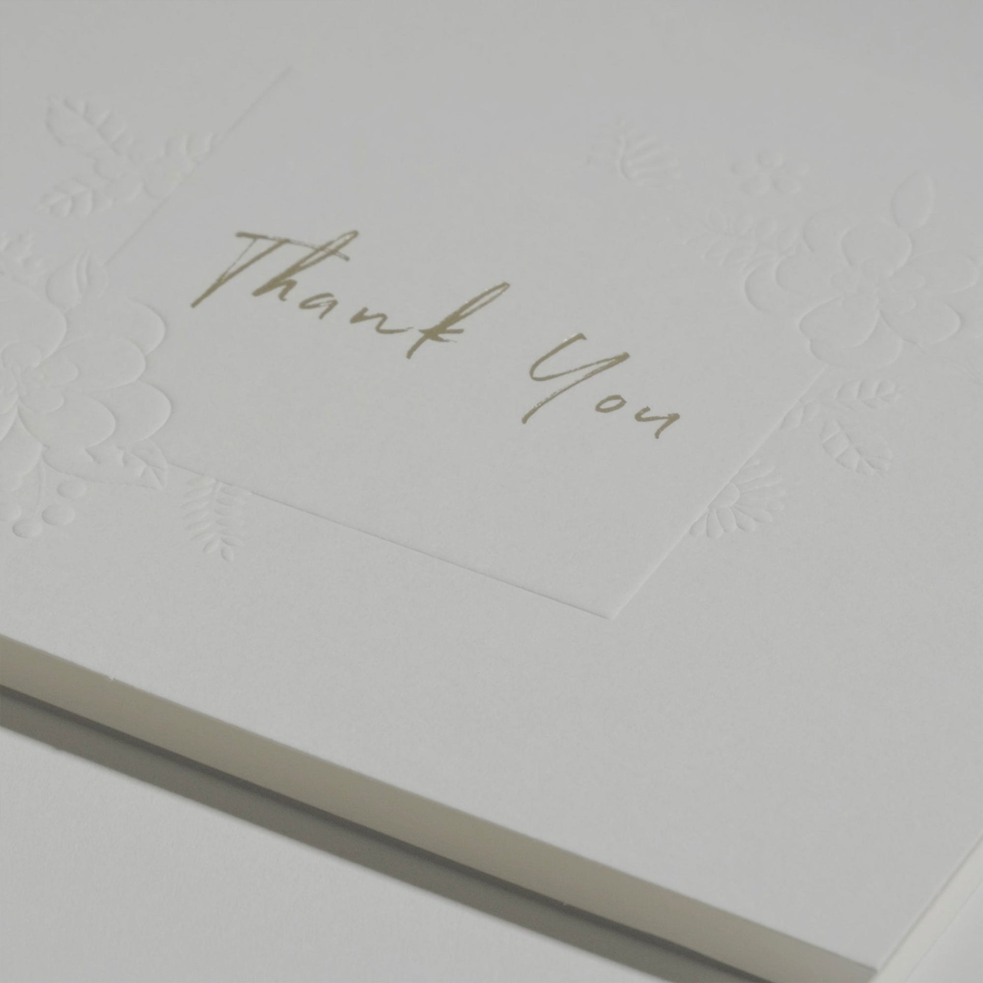 Side angle close-up emphasizing the crisp cursive typography and premium embossed floral details on a luxury corporate thank you note.