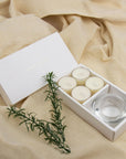 Premium Vaucluse vanilla tealight candles and heavy glass holder set nestled on an aesthetic, softly draped neutral linen background with rosemary.