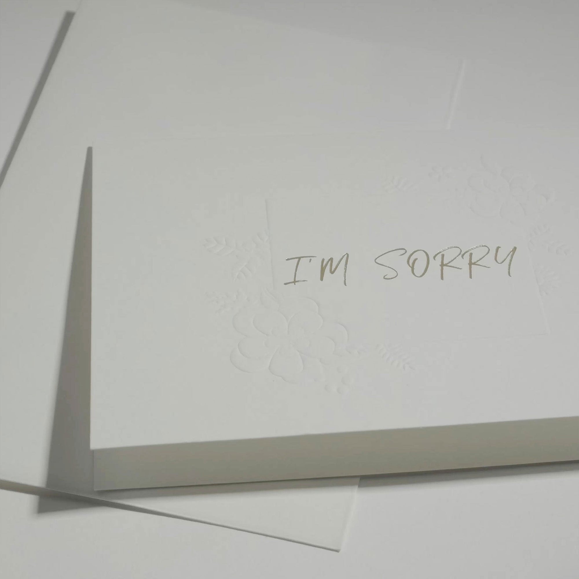 Side angle close-up focusing on the elegant embossed floral framework around the "I'm Sorry" text on premium white cardstock.
