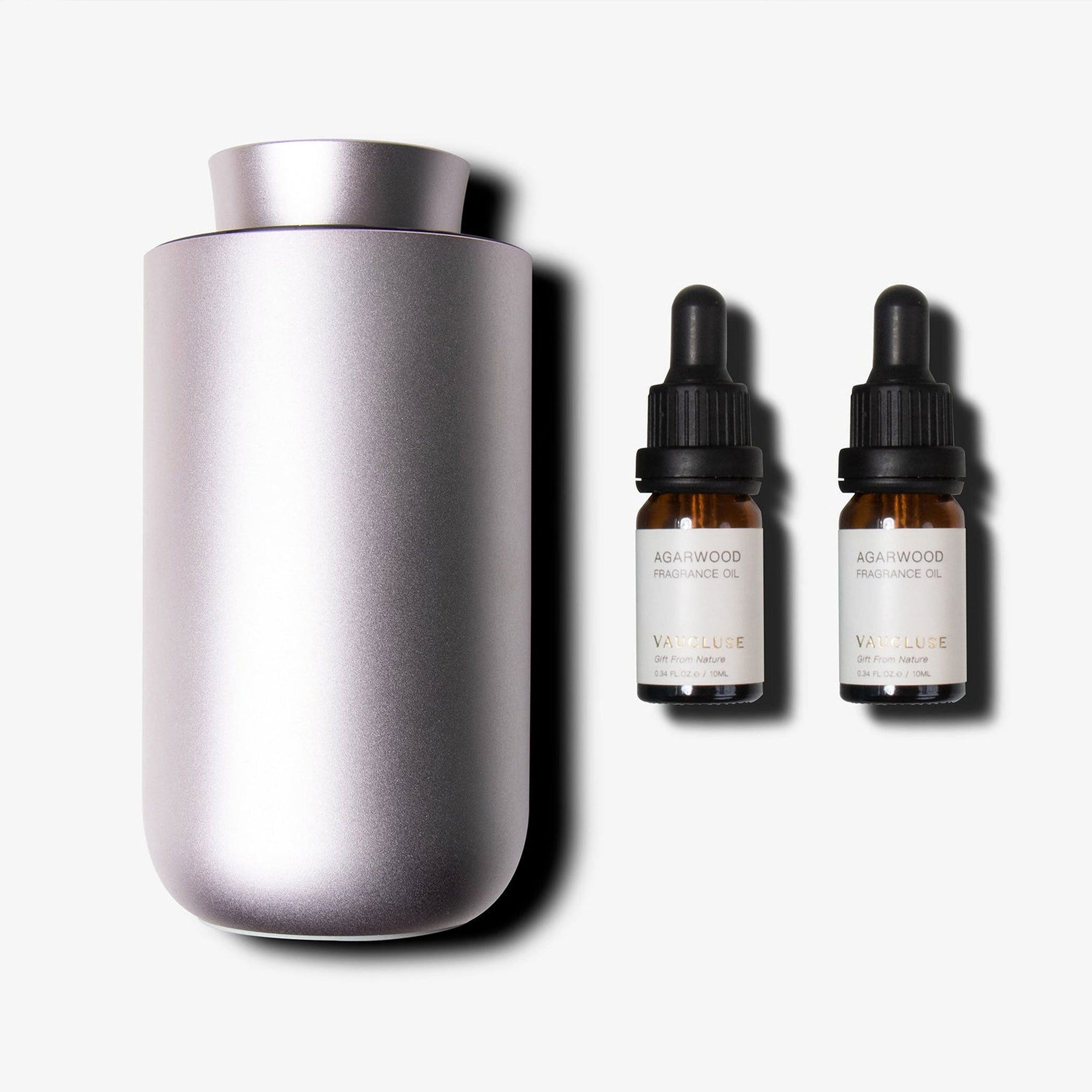 A brushed purple dusk waterless nebulizing diffuser placed next to two amber glass essential oil dropper bottles with black caps.