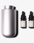 A brushed purple dusk waterless nebulizing diffuser placed next to two amber glass essential oil dropper bottles with black caps.