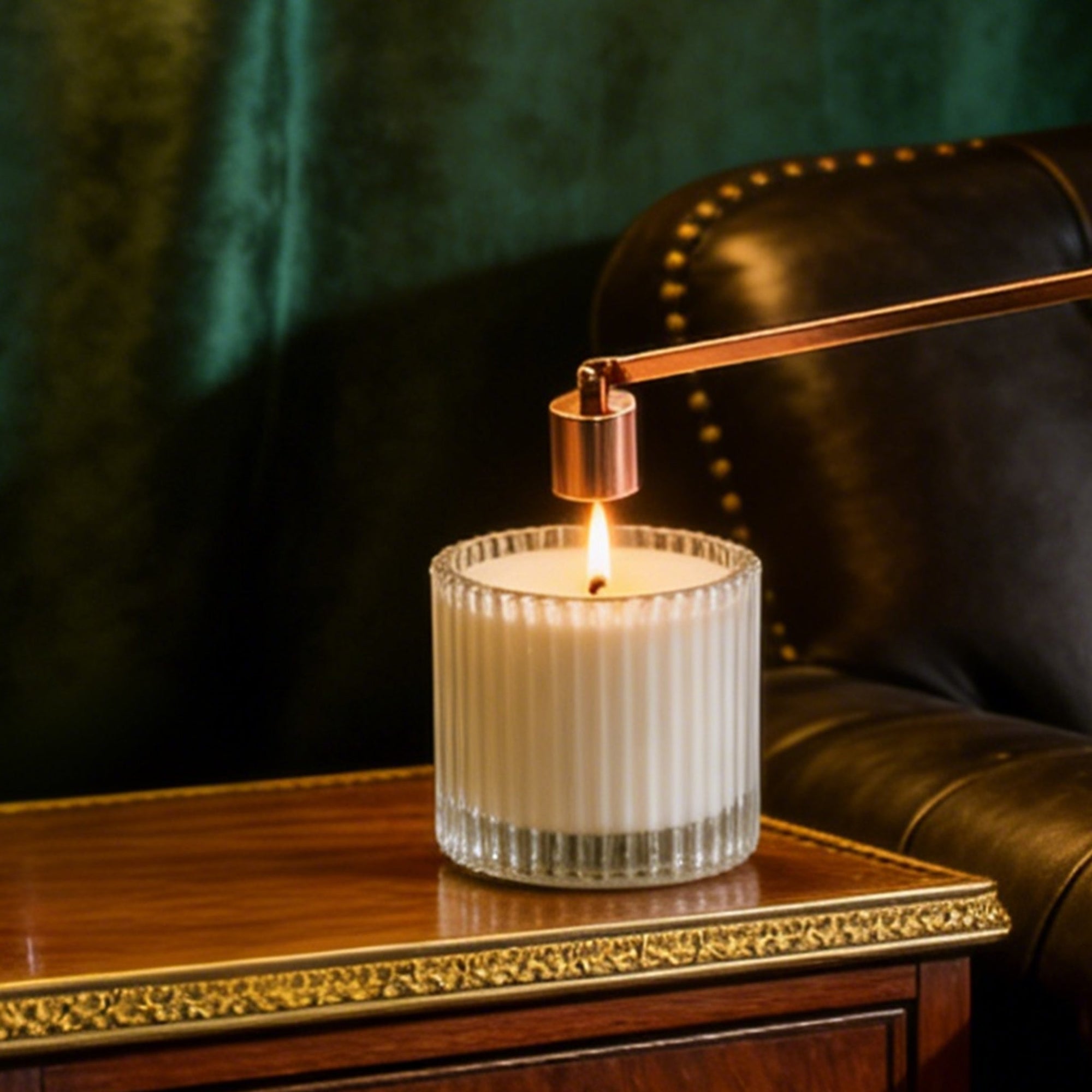 A modern rose gold bell candle snuffer being used to safely extinguish a burning candle flame on a wooden desk.
