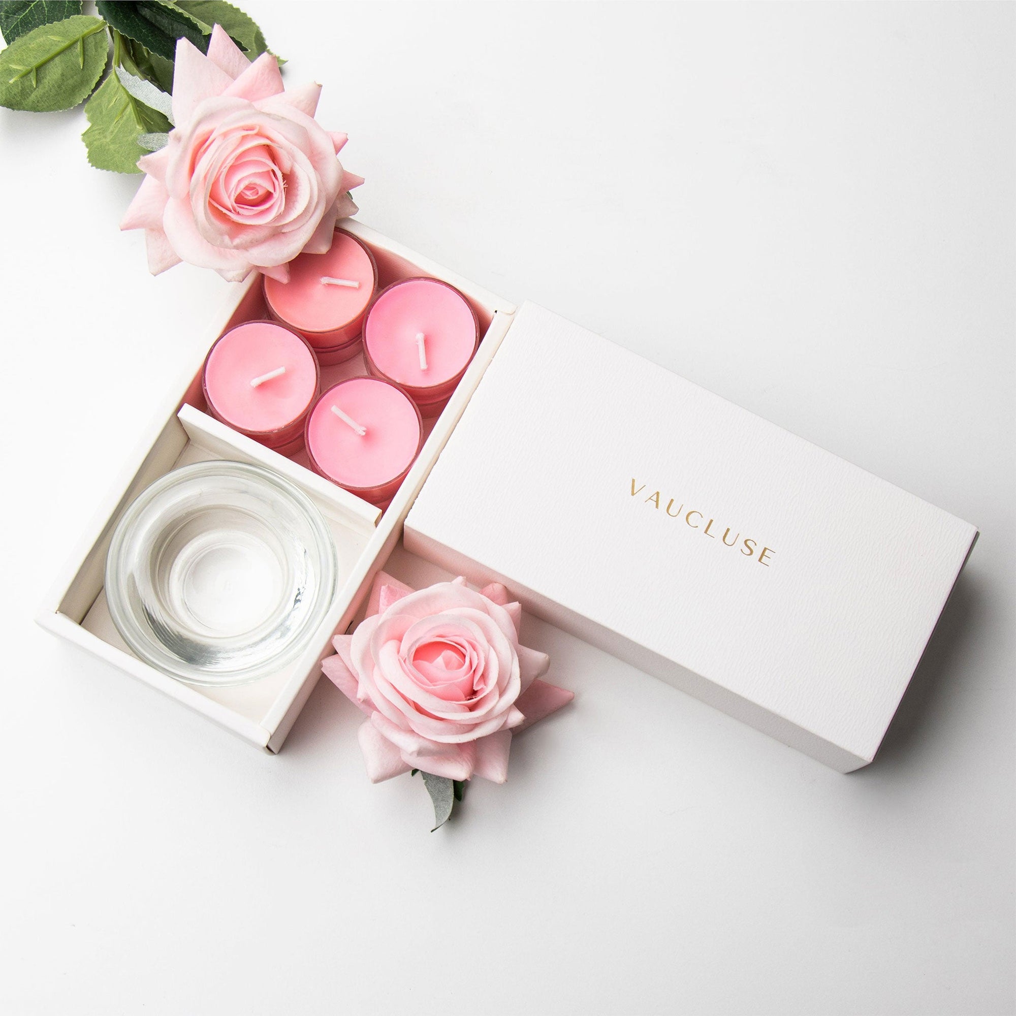 Top-down minimalist flat lay of the open pink rose tealight candle set beautifully accessorized with fresh pink rose blossoms on a white background.