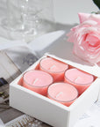 Close-up view of the premium white Vaucluse sliding packaging revealing a tiered 16-pack tray of pink rose scented tealight candles next to an elegant rose blossom.