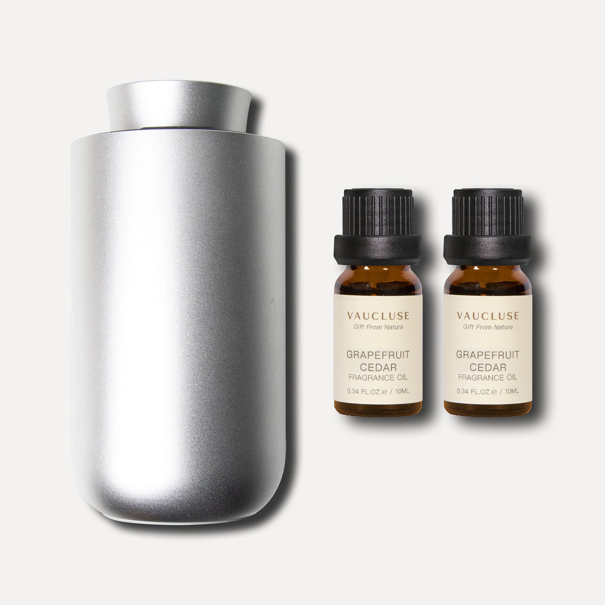 A matte silver waterless nebulizing aroma diffuser positioned alongside a pair of 10ml Vaucluse grapefruit cedar essential oil bottles.