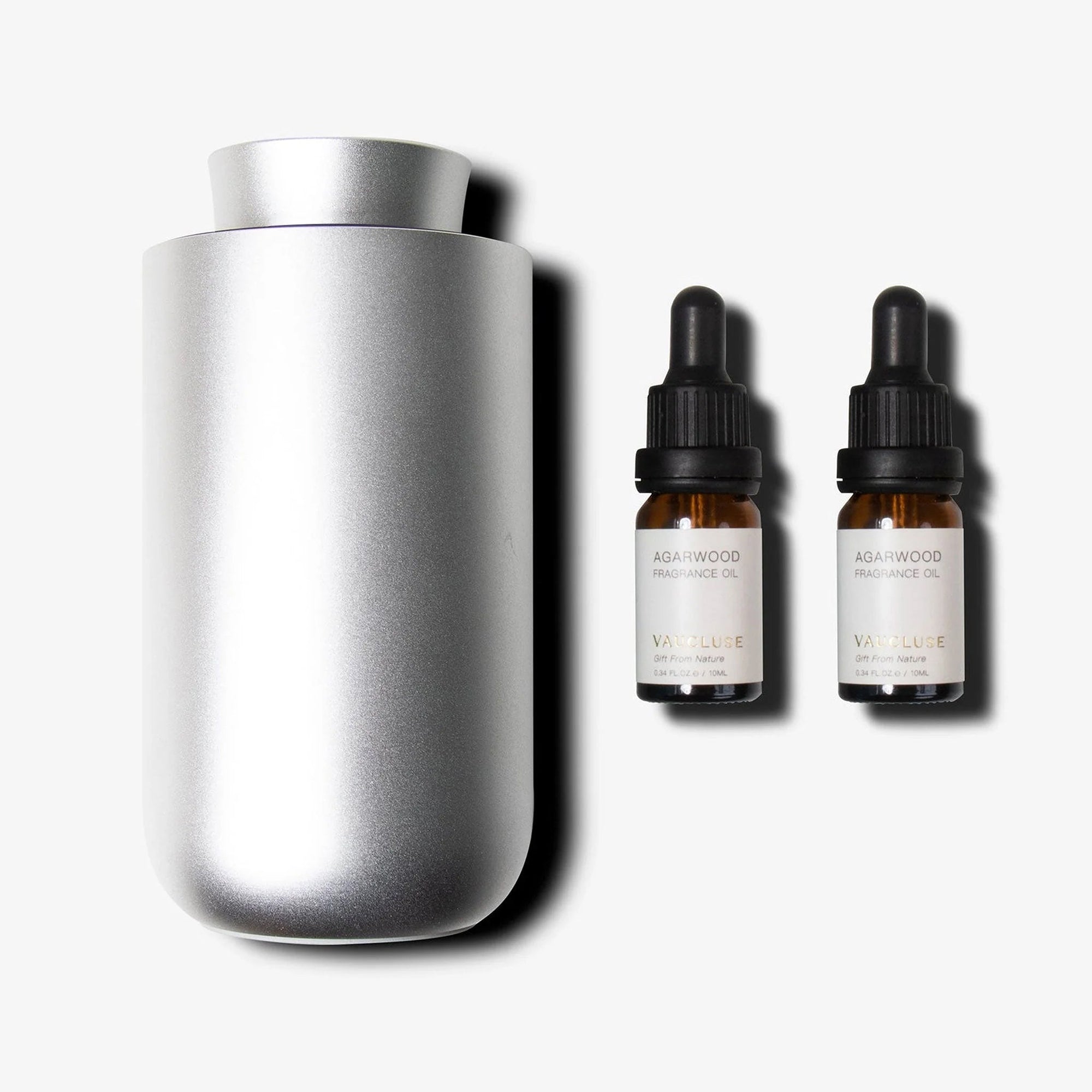 A brushed silver waterless nebulizing diffuser standing next to two amber glass essential oil dropper bottles with dropper tops.
