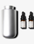 A brushed silver waterless nebulizing diffuser standing next to two amber glass essential oil dropper bottles with dropper tops.