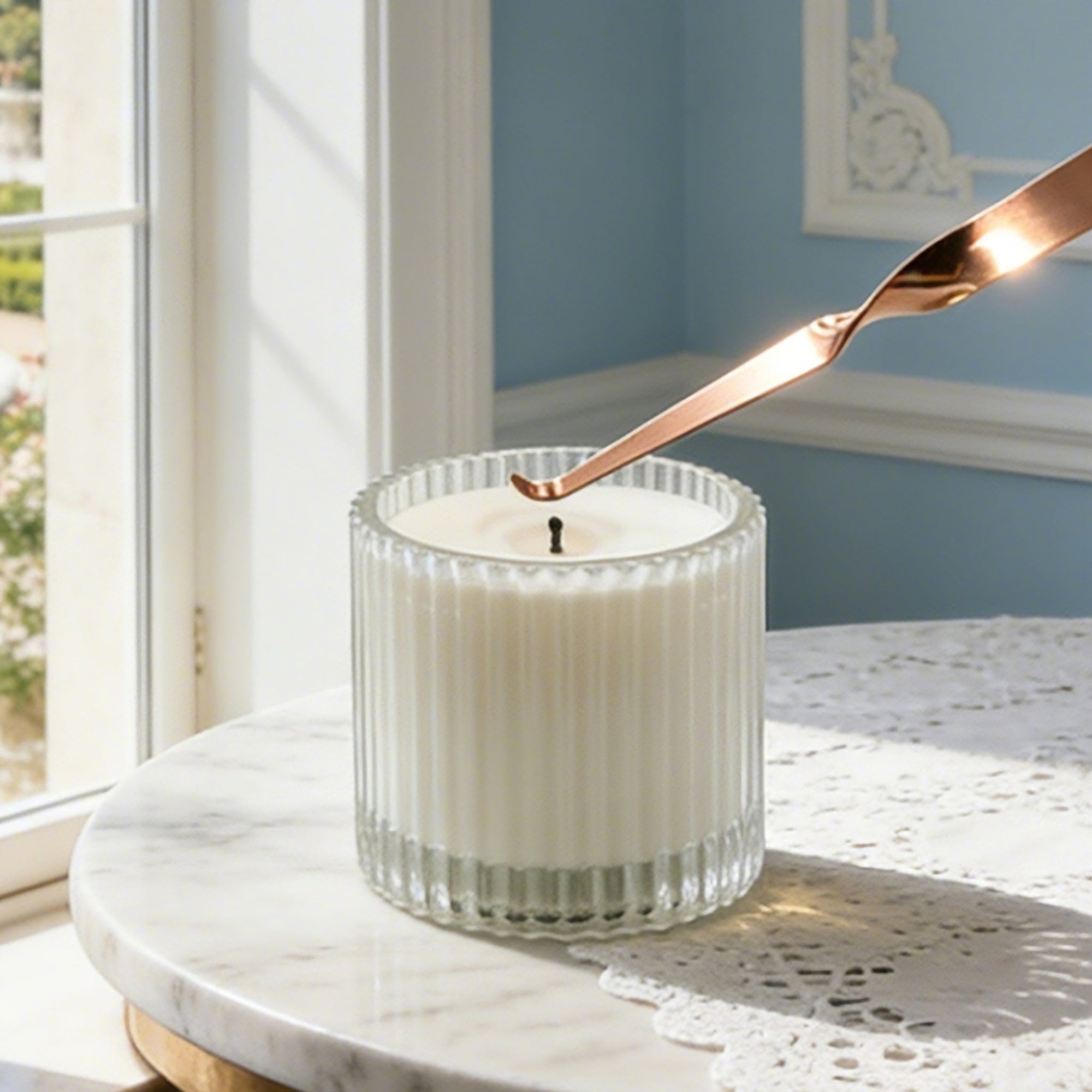 Adjusting a candle wick using a polished rose gold candle wick dipper tool on a round marble tabletop.