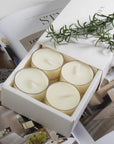 Close-up view of the premium white Vaucluse sliding packaging revealing a tiered 16-pack tray of vanilla scented tealight candles styled next to a fresh sprig of rosemary.