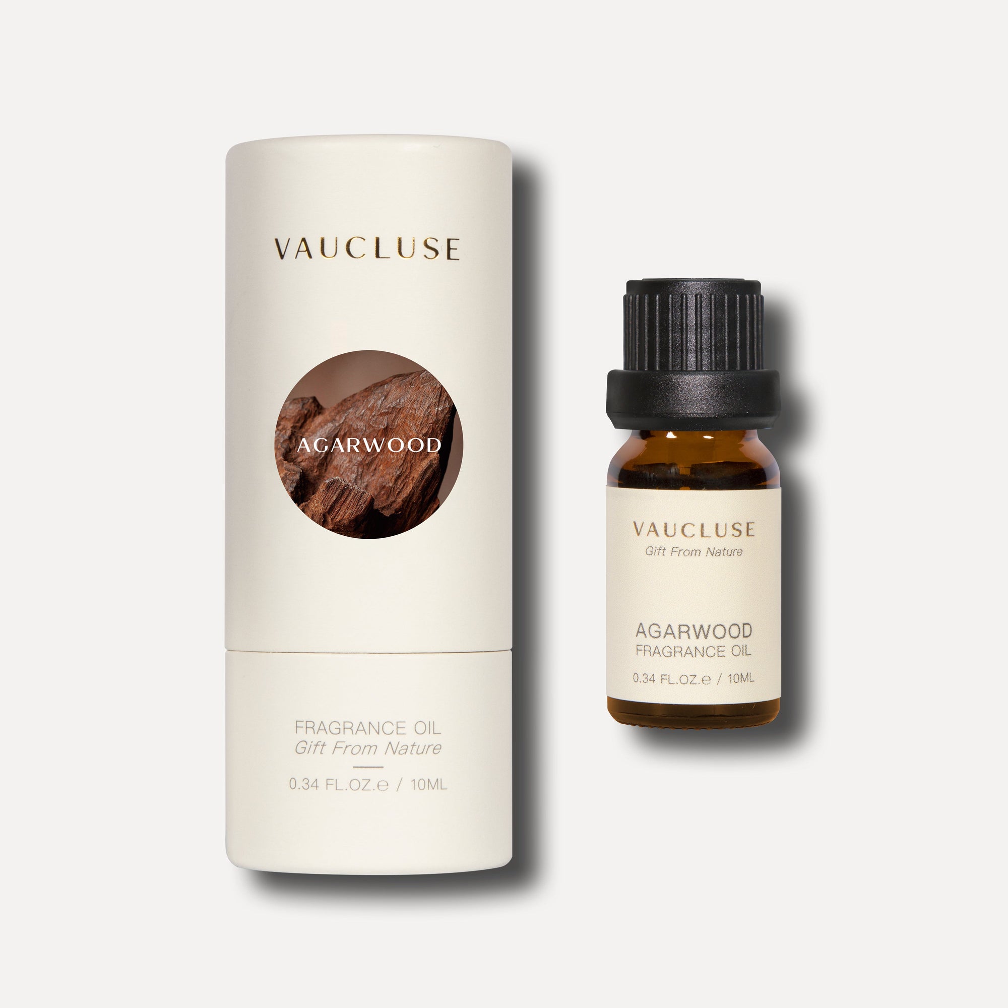 A 10ml bottle of agarwood essential oil standing next to its elegant white cylindrical tube packaging featuring a circular wood grain design.