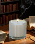 A lit Vaucluse Black Rose luxury scented candle with trailing smoke, resting on a warm wooden desk next to vintage books.