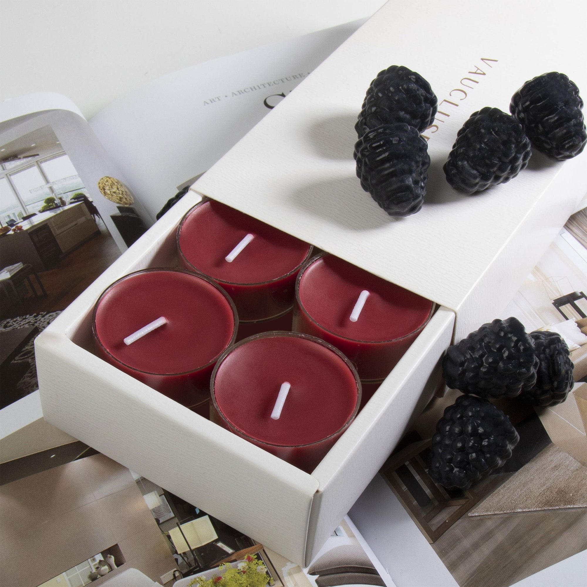 A deep purple blackberry scented tealight candle in a clear glass holder shown in the foreground with fresh blackberries resting on a partial view of the sliding box tray.