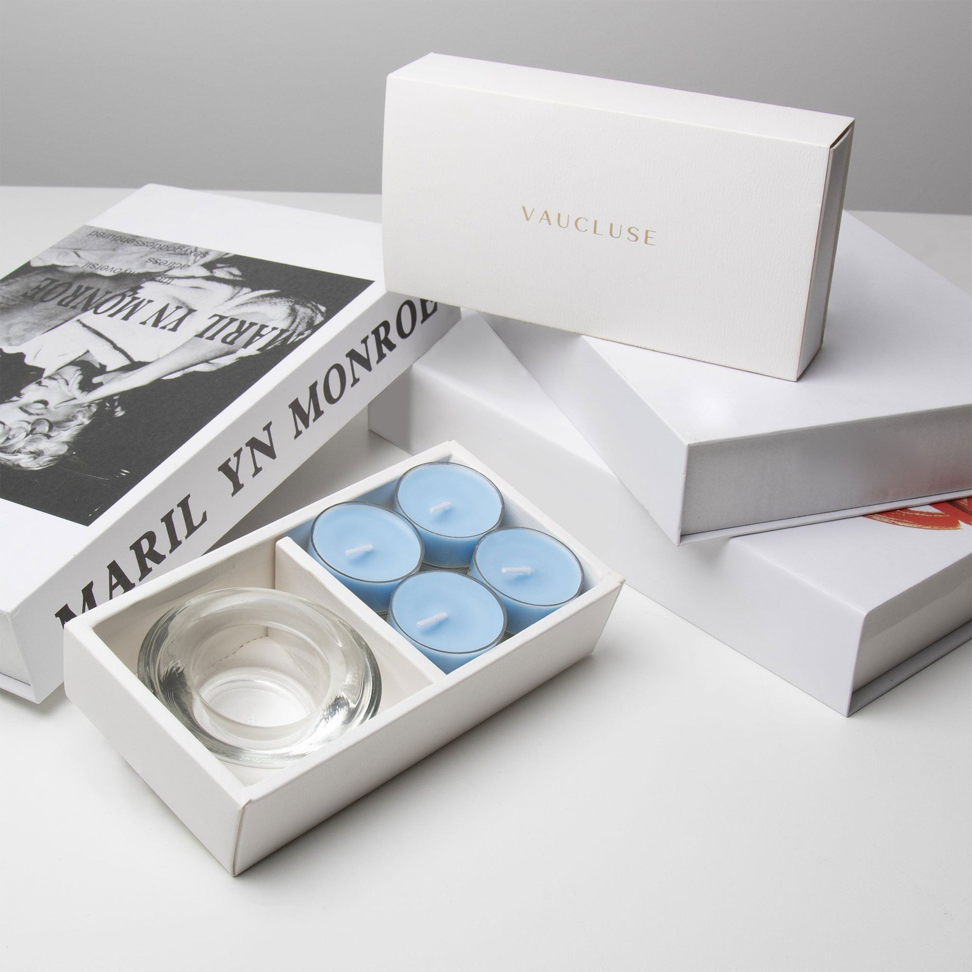 Premium retail unboxing display featuring the open light blue breeze tealight set resting against stacked white gift boxes with gold branding.