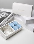 Premium retail unboxing display featuring the open light blue breeze tealight set resting against stacked white gift boxes with gold branding.
