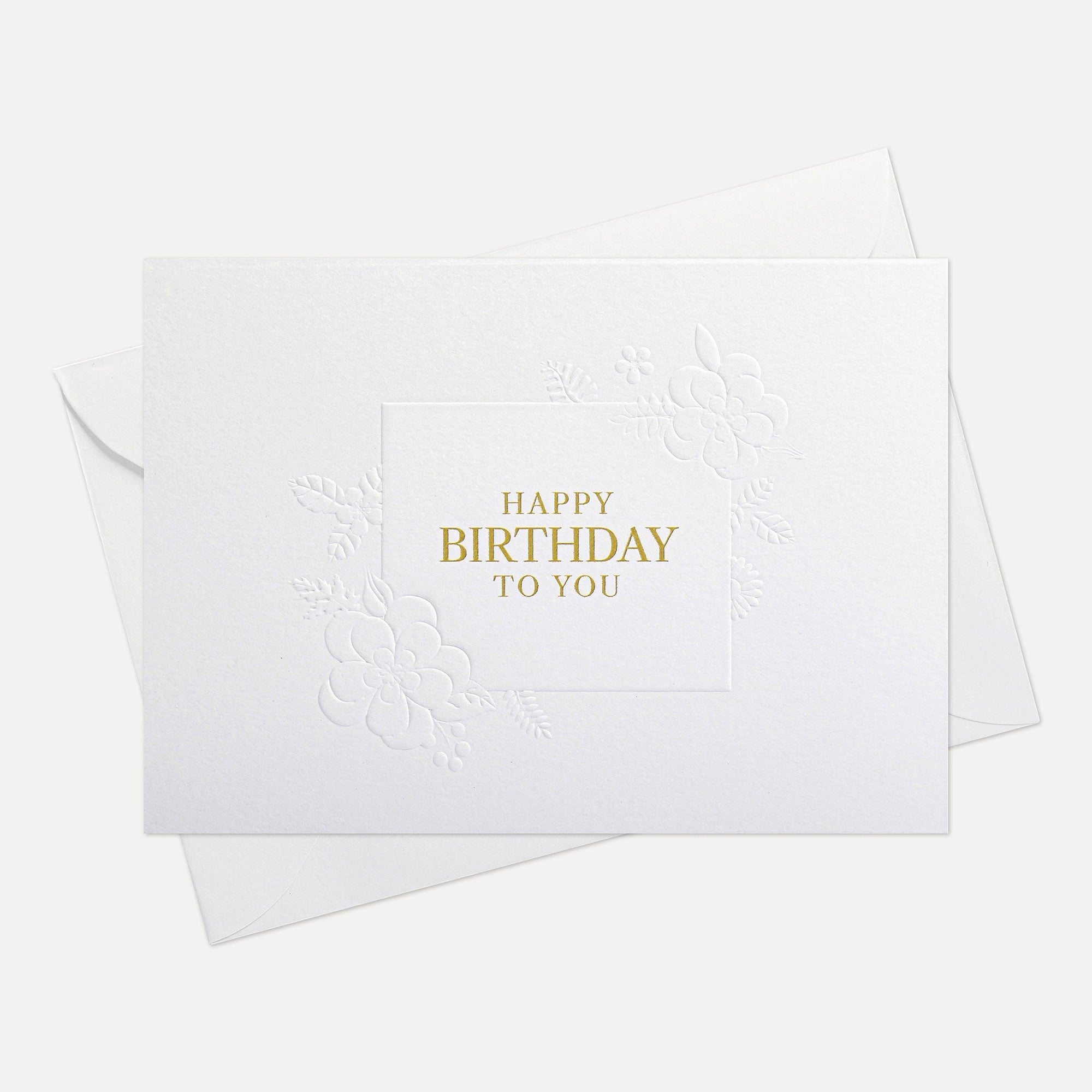 Overhead view of a minimalist luxury white birthday greeting card featuring gold foil text "Happy Birthday To You" paired with a matching white paper envelope.