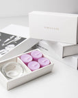 Premium brand unboxing layout showing the open lavender tealight set against a clean backdrop of stacked white luxury gift boxes with gold foil branding.