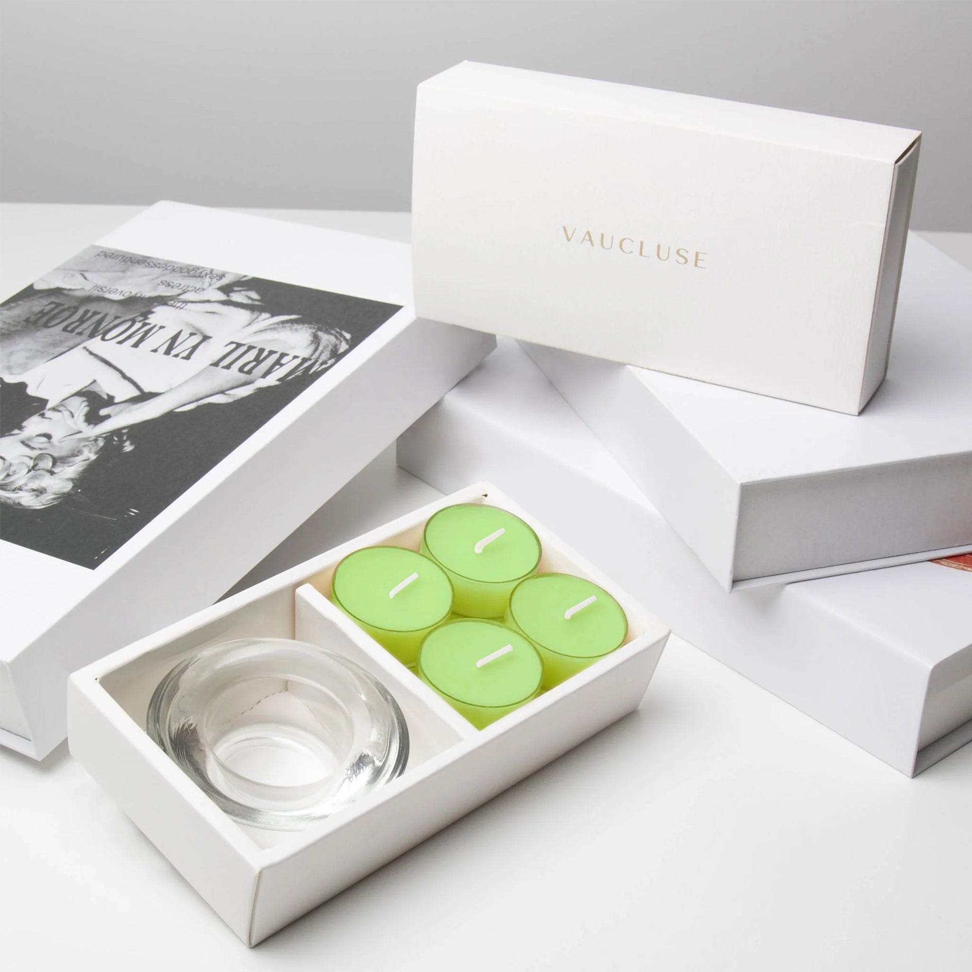 Premium editorial unboxing scene featuring the open lily tealight candle set arranged neatly next to stacked luxury white gift boxes with gold foil branding.