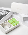 Premium editorial unboxing scene featuring the open lily tealight candle set arranged neatly next to stacked luxury white gift boxes with gold foil branding.
