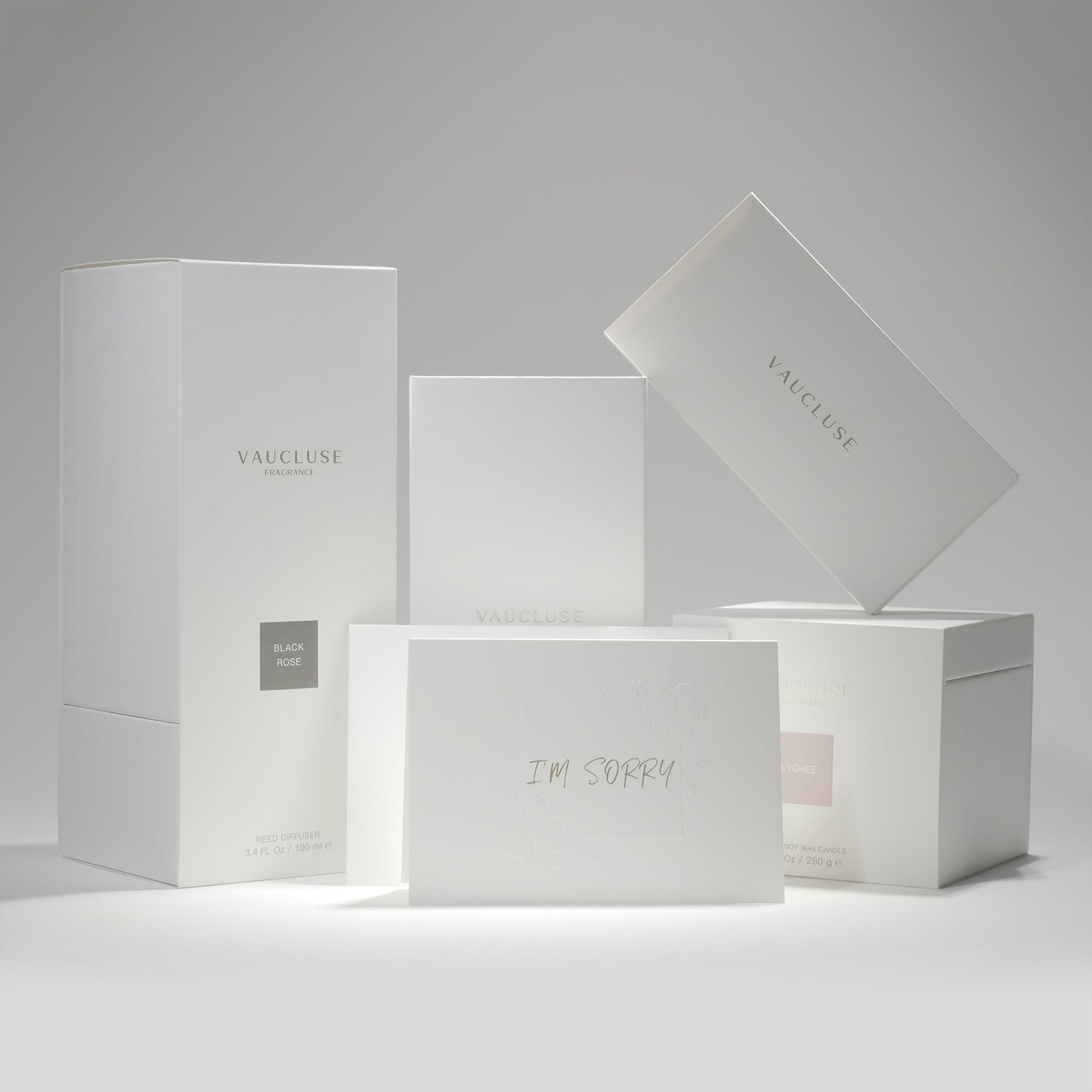 A curated stack of premium white Vaucluse fragrance gift packaging boxes and candle boxes arranged alongside the minimalist "I'm Sorry" greeting card.