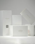 A curated composition of sleek white Vaucluse fragrance boxes, premium gift packaging, and the minimalist luxury birthday greeting card arranged together.