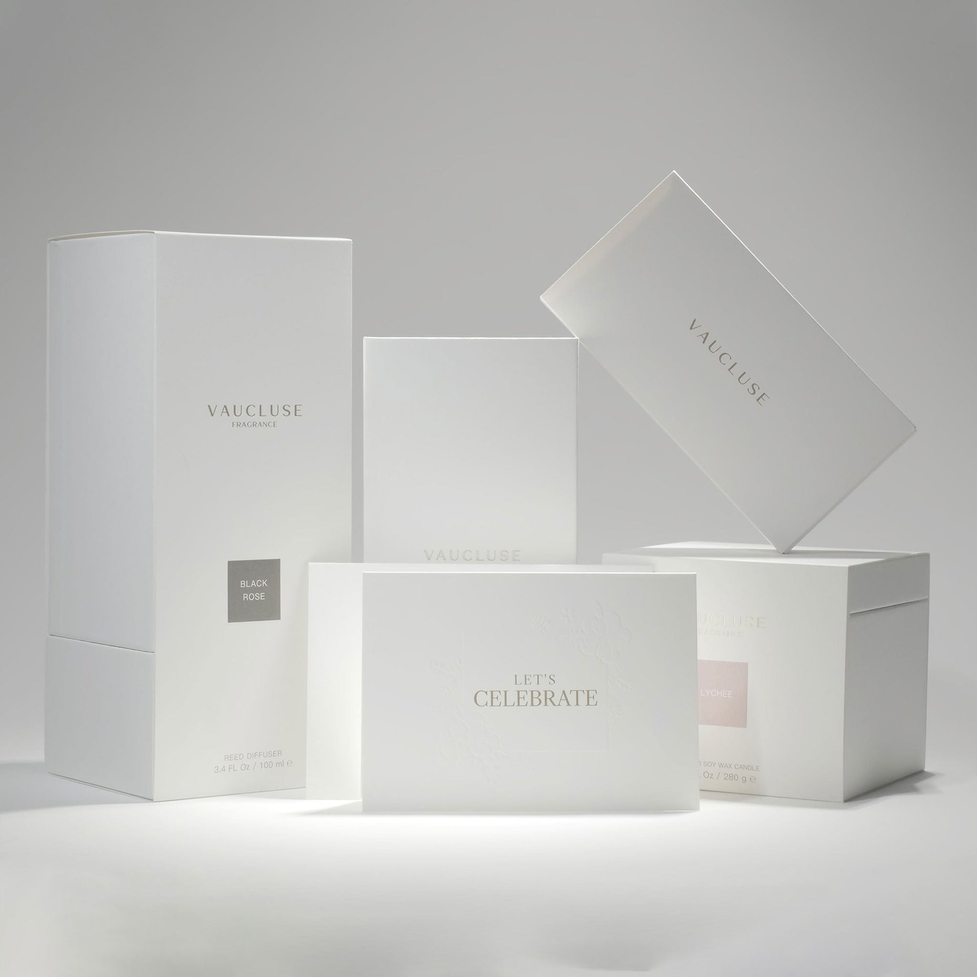 A curated collection of premium minimalist white Vaucluse fragrance boxes, candle packaging, and the elegant Let's Celebrate card arranged neatly on a crisp white surface.