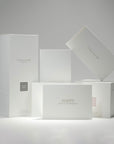 A curated collection of premium minimalist white Vaucluse fragrance boxes, candle packaging, and the elegant Happy House Warming card arranged neatly on a crisp white surface.