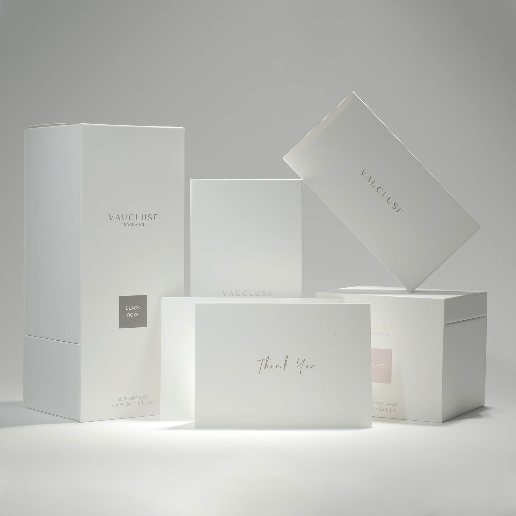 A curated collection of premium minimalist white Vaucluse fragrance boxes, candle packaging, and the elegant thank you card neatly arranged on a white surface.