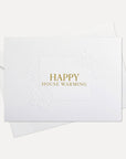 Front flat lay view of a minimalist luxury white housewarming card featuring elegant gold text reading Happy House Warming, displayed with its matching white envelope.